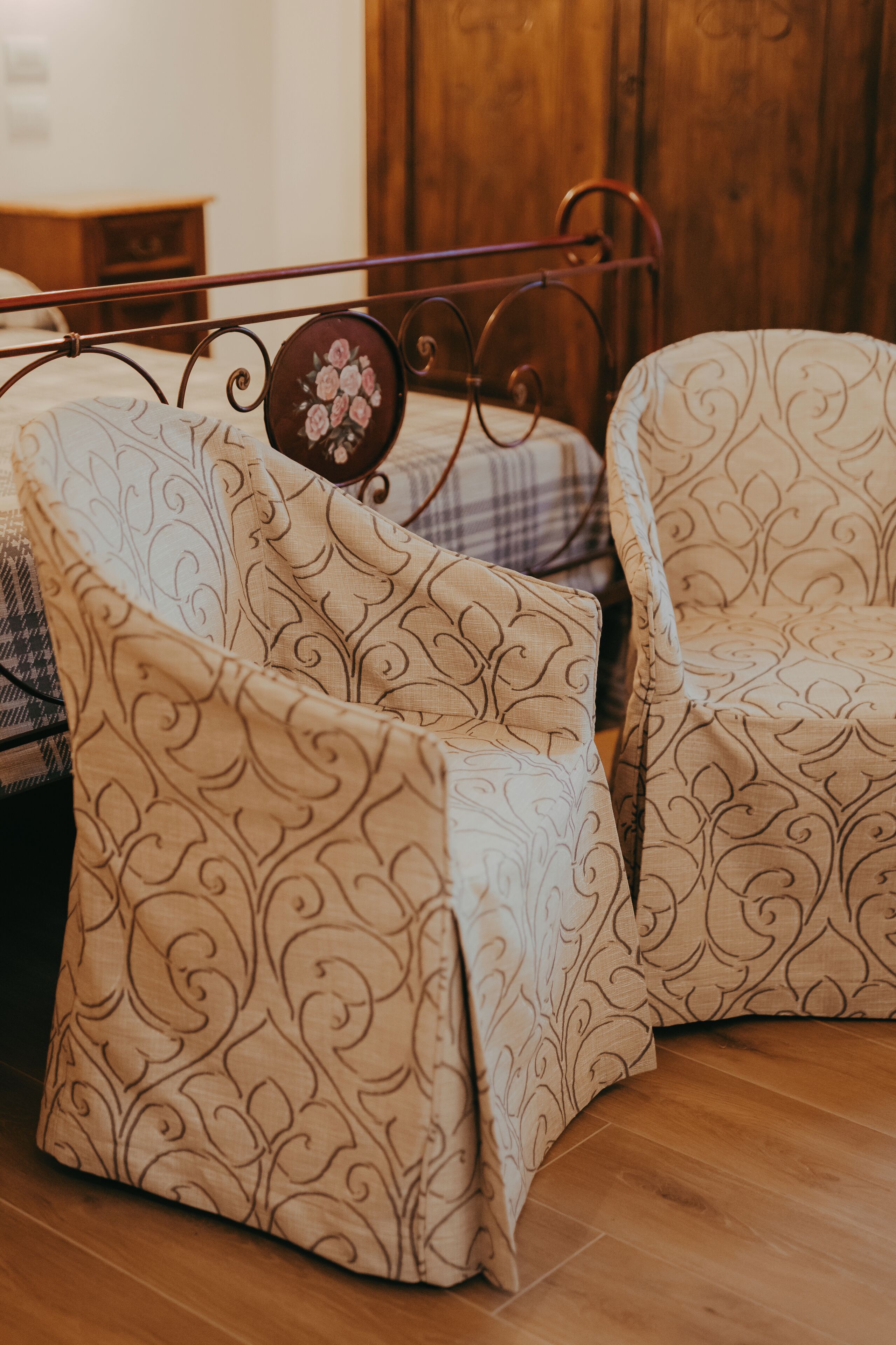 A bed with a metal frame and floral headboard, flanked by two patterned armchairs.