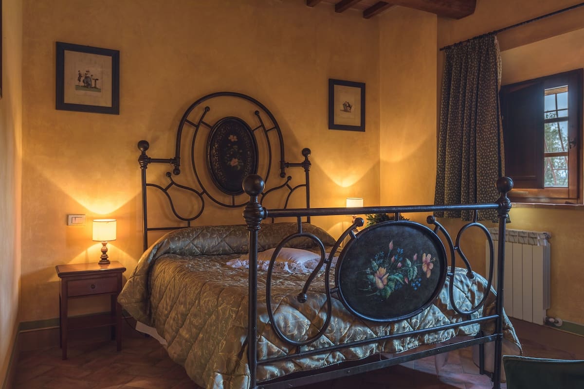 A bedroom with a metal bed frame, a bedside table with a lamp, and a window with curtains.
