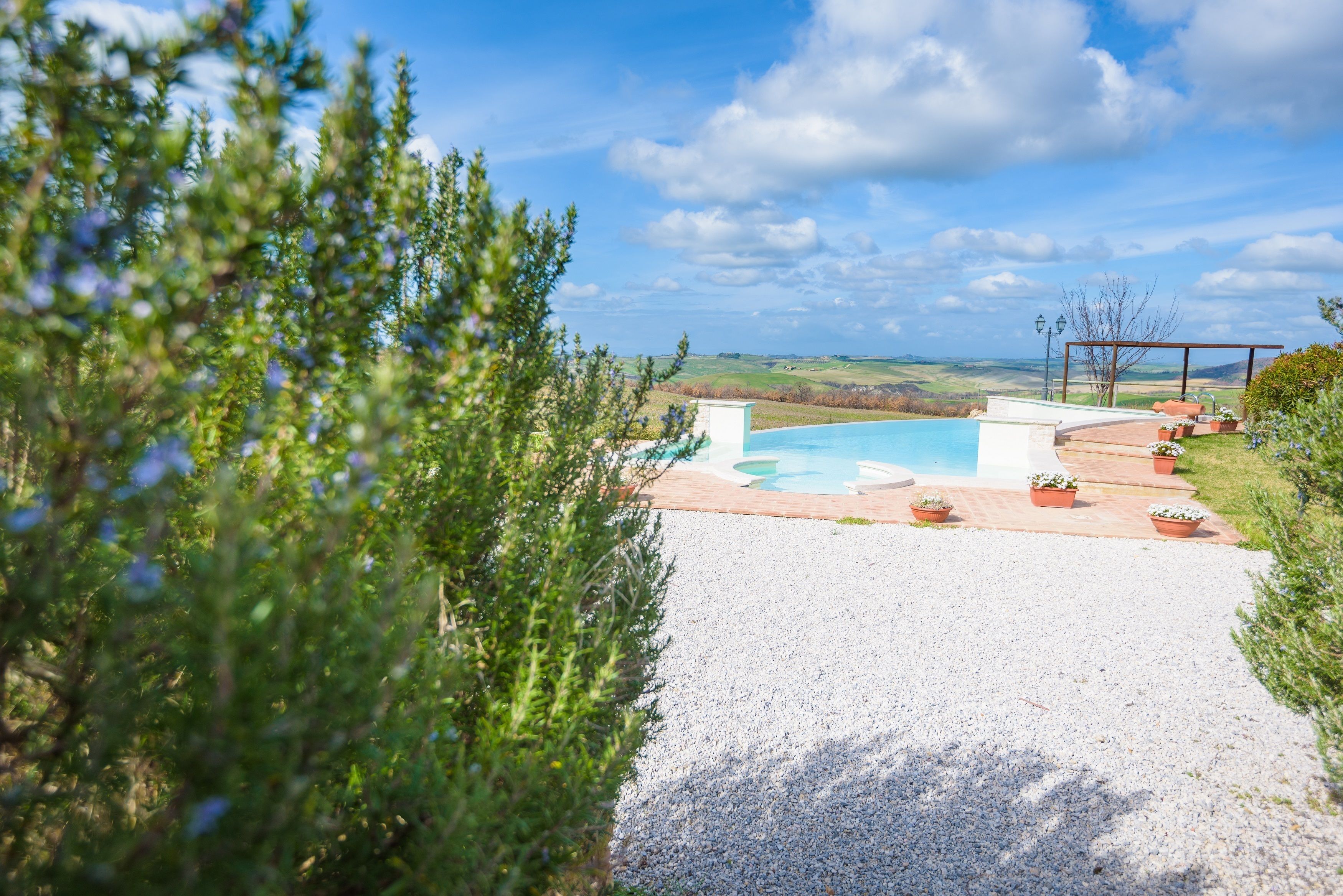 A pool area with a view of rolling hills, surrounded by gravel and potted plants.