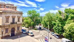 A street view with parked cars, a building with a classical facade, and trees.