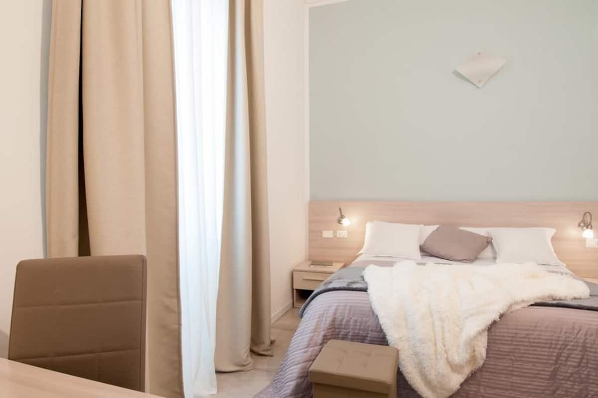 Un dormitorio con cama, mesitas de noche, una silla y cortinas.