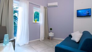 A modern room with a blue sofa, a small side table, a TV, and a window with curtains.