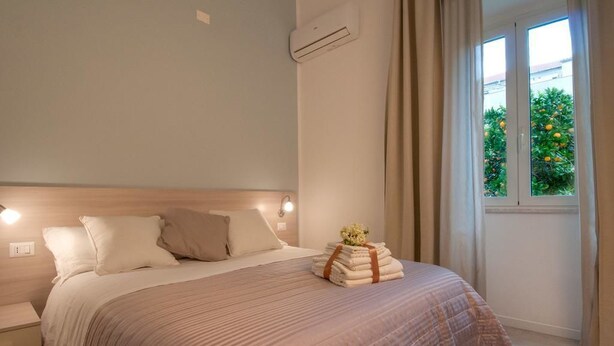 A bedroom with a bed, bedside tables, a window with curtains, and a view of greenery outside.