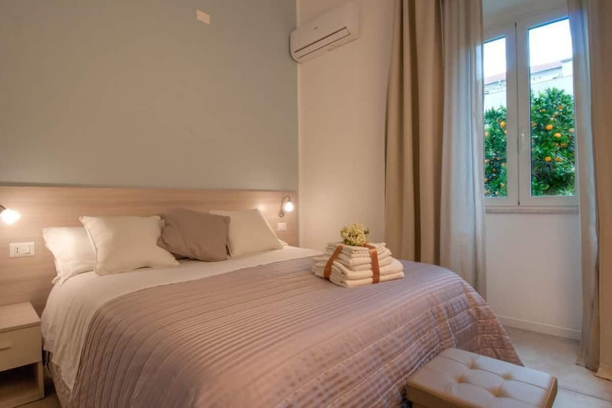 Un dormitorio con cama, mesitas de noche, ventana con cortinas y vista a zonas verdes.