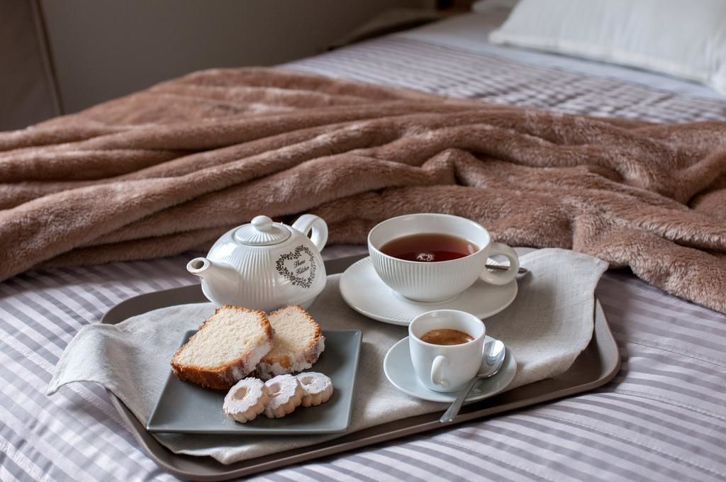 Un vassoio con un teiera, una tazza di tè, una tazza di caffè e dolci su un letto con una coperta a righe.