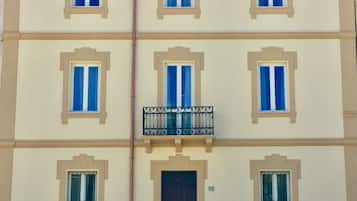 Un edificio a più piani con sei finestre per ogni piano, un portone centrale e un piccolo balcone con ringhiera metallica.