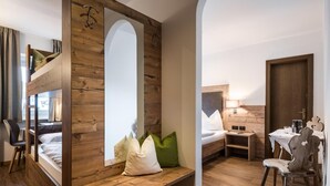 Una habitación con una cama nido, paneles de madera en la pared, un escritorio con una silla, una mesa con una lámpara y una puerta.
