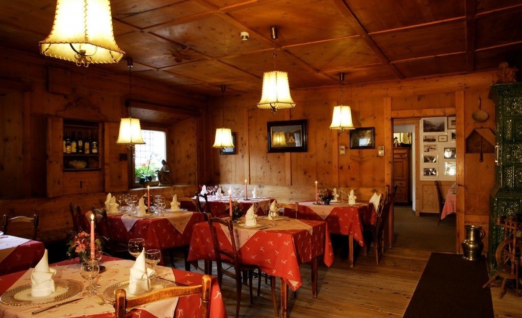 A cozy restaurant with wooden walls and tables set with red tablecloths and candles.