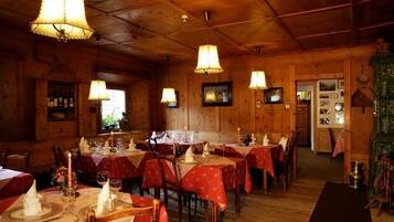 A cozy restaurant with wooden walls and tables set with red tablecloths and candles.