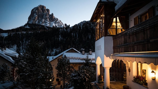 Una montaña cubierta de nieve con una edificación de estilo chalet que tiene un balcón con luces, un tejado nevado y vistas a la montaña.