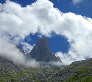 A mountain peak with a rugged, rocky foreground and a clear blue sky with clouds. - Casa Asprón (Cangas de Onis)