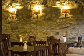 A restaurant with stone walls, wooden tables, and chairs. There are two pendant lights hanging from the ceiling. - Casa Asprón (Cangas de Onis)