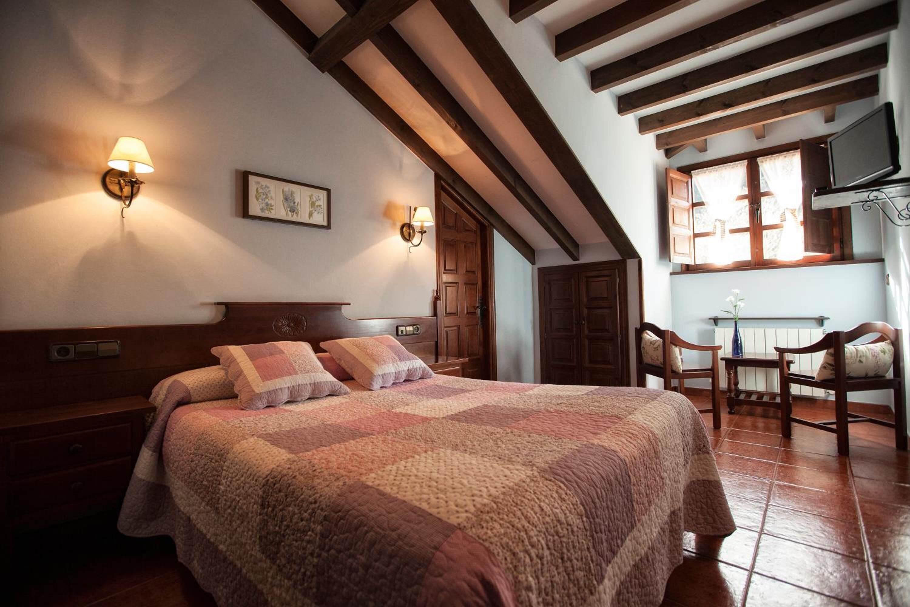 A cozy bedroom with a large bed, wooden headboard, two wall-mounted lamps, and a window with curtains.