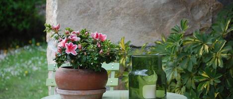A green metal table with a terracotta pot containing pink flowers and a green glass candle holder.