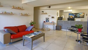 Un salon moderne avec un canapé rouge, une table basse avec des livres, un bureau avec un ordinateur et un téléviseur.