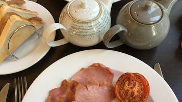 Desayuno con platos de huevos, tocino, salchichas, champiñones, morcilla y tostadas. También hay teteras y una taza de té.