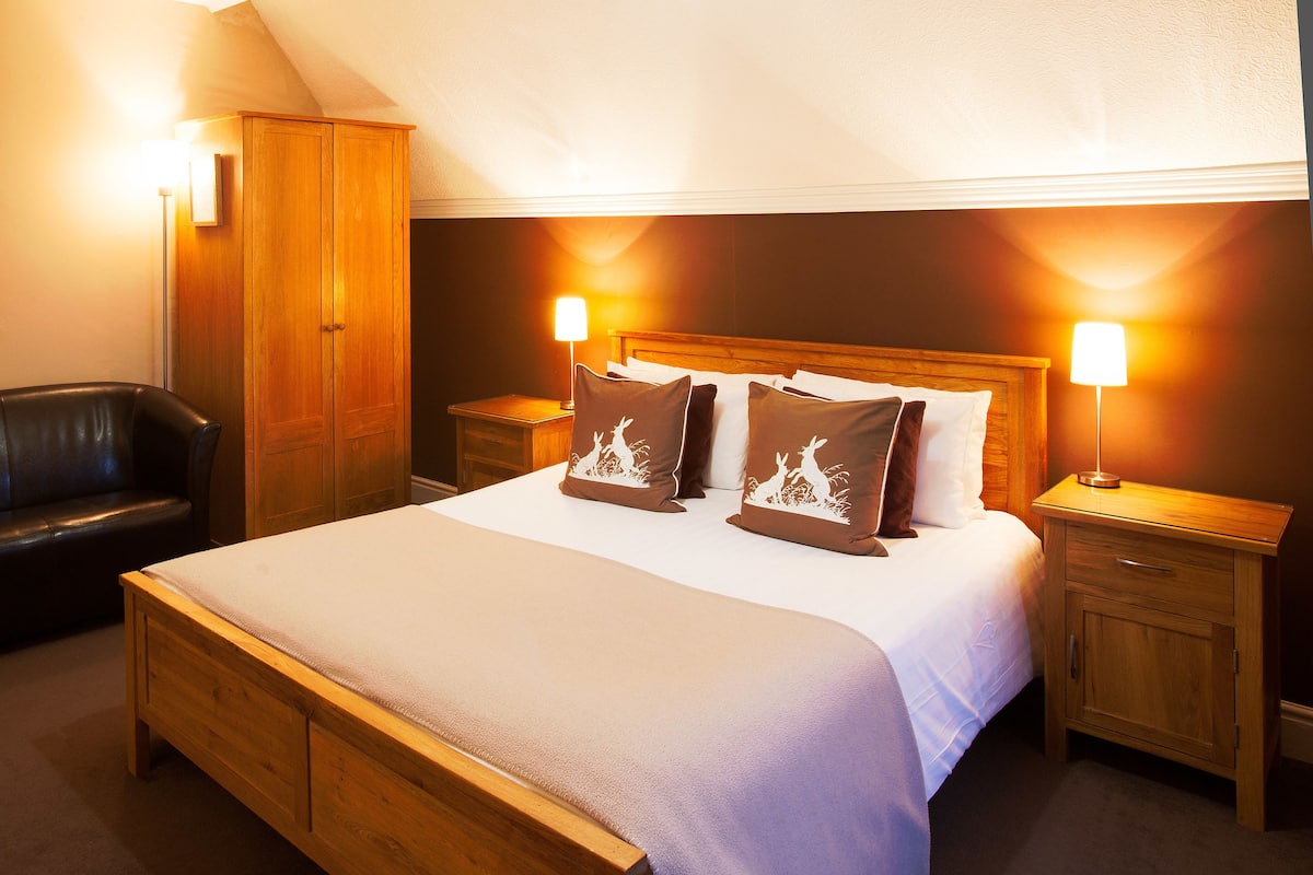 Une chambre à coucher avec un lit en bois, un fauteuil en cuir, une armoire et des lampes de chevet.