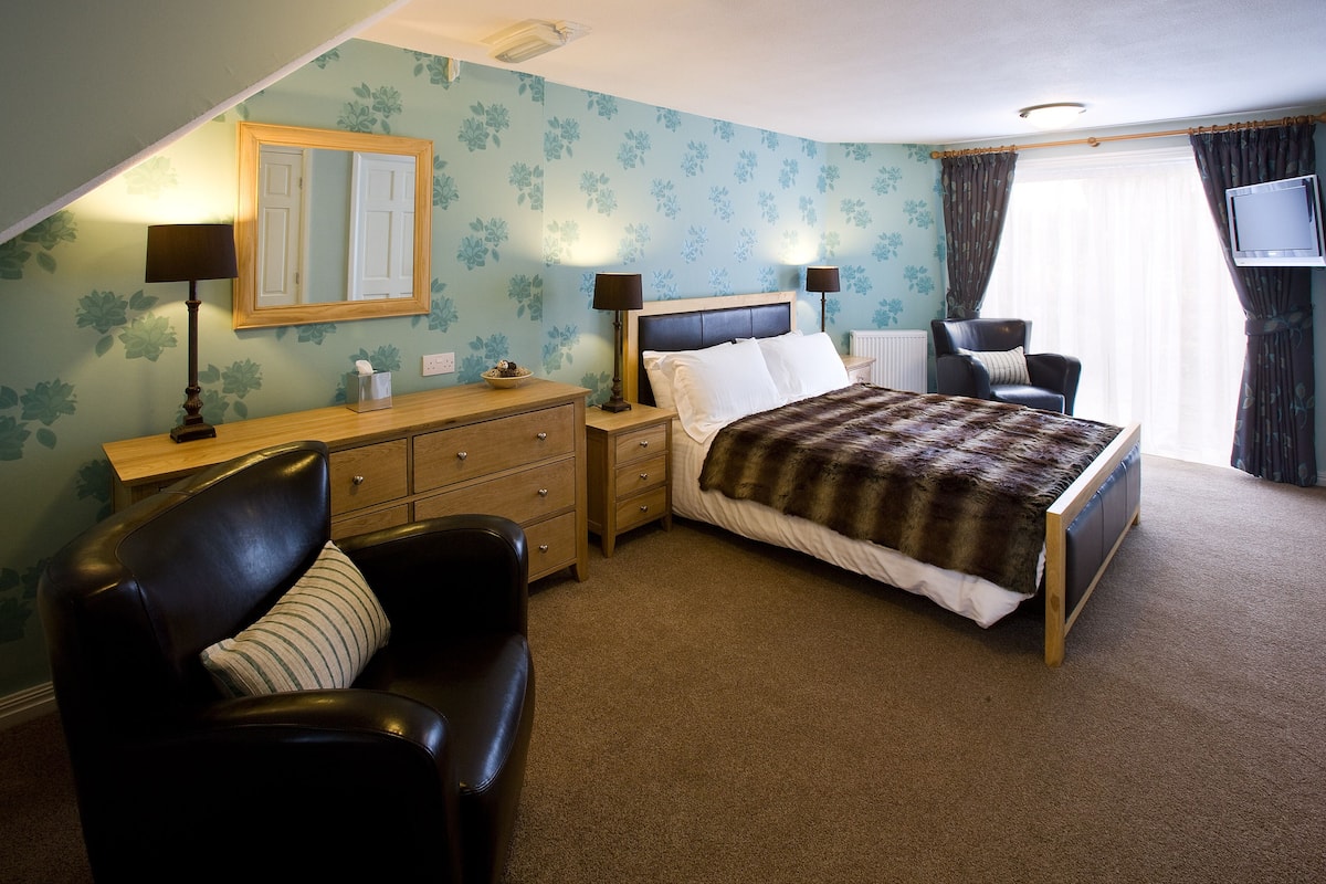 Une chambre à coucher comprenant un lit, une table de chevet, une commode, une chaise et un téléviseur.