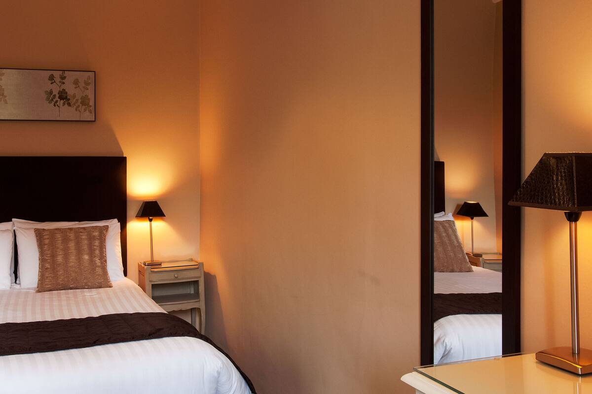 Une chambre d’hôtel avec un grand lit, deux tables de chevet, une commode, un miroir et une œuvre d’art accrochée au mur.