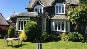 Une grande maison en pierre, dotée de nombreuses cheminées, avec une pelouse bien entretenue et une petite table et quelques chaises disposées dans le jardin.