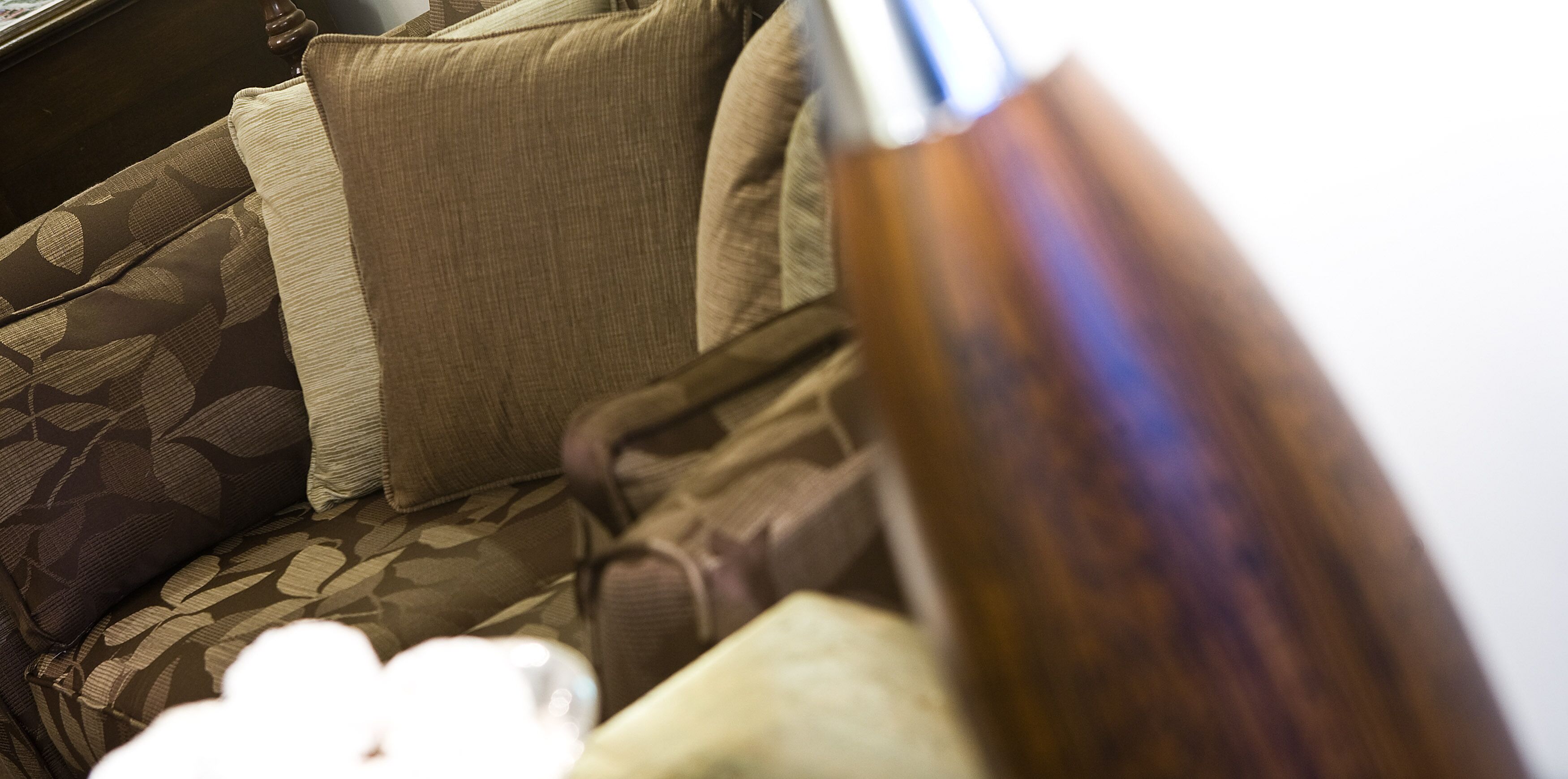 A close-up of a patterned sofa with a cushion and a wooden object, possibly a vase or a lamp.