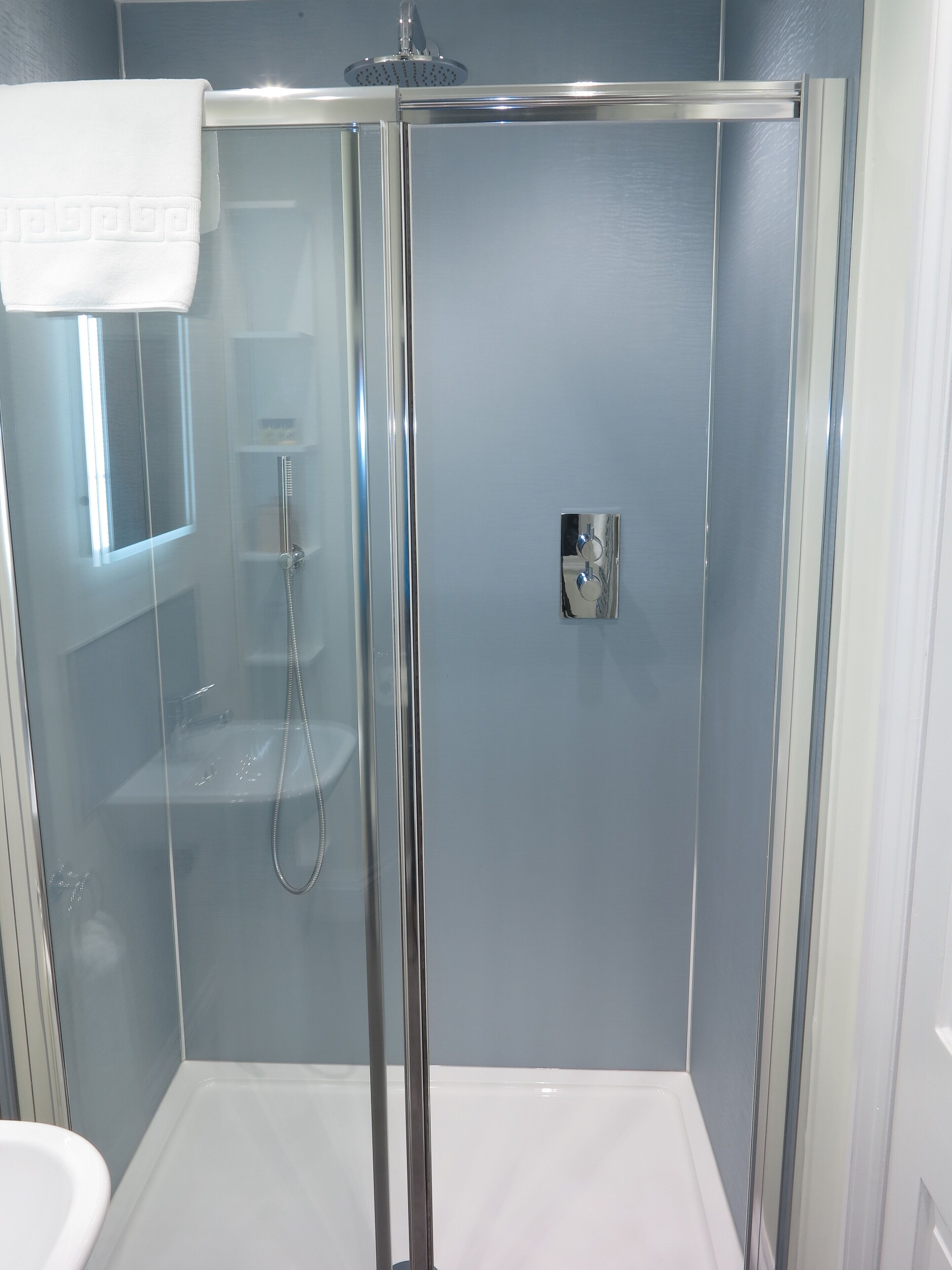 A glass-enclosed shower stall with a chrome showerhead and a handheld shower attachment.