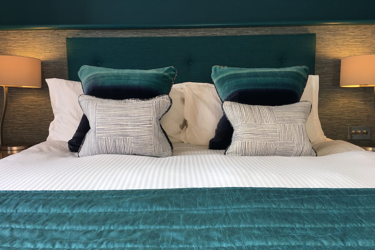 Un lit bien fait, avec une literie à rayures, deux oreillers et un plaid de couleur turquoise.
