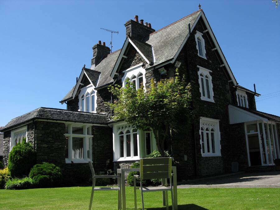 A large stone house with multiple chimneys, white-framed windows, and a well-maintained lawn.