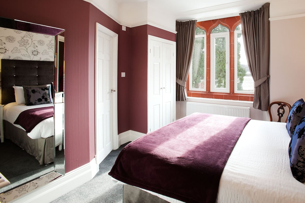 Une chambre d’hôtel avec un lit, un miroir, une fenêtre avec des rideaux et une lampe.