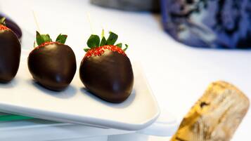 A bottle of champagne with a label, ice cubes, and three chocolate-covered strawberries with skewers.
