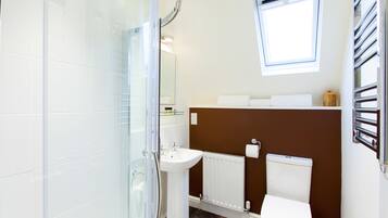 A bathroom with a glass shower enclosure, a sink, a toilet, and a window above the sink.