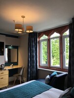 Ein Schlafzimmer mit Bett, Schreibtisch, Stuhl, Kommode und einem Fenster mit Vorhängen.