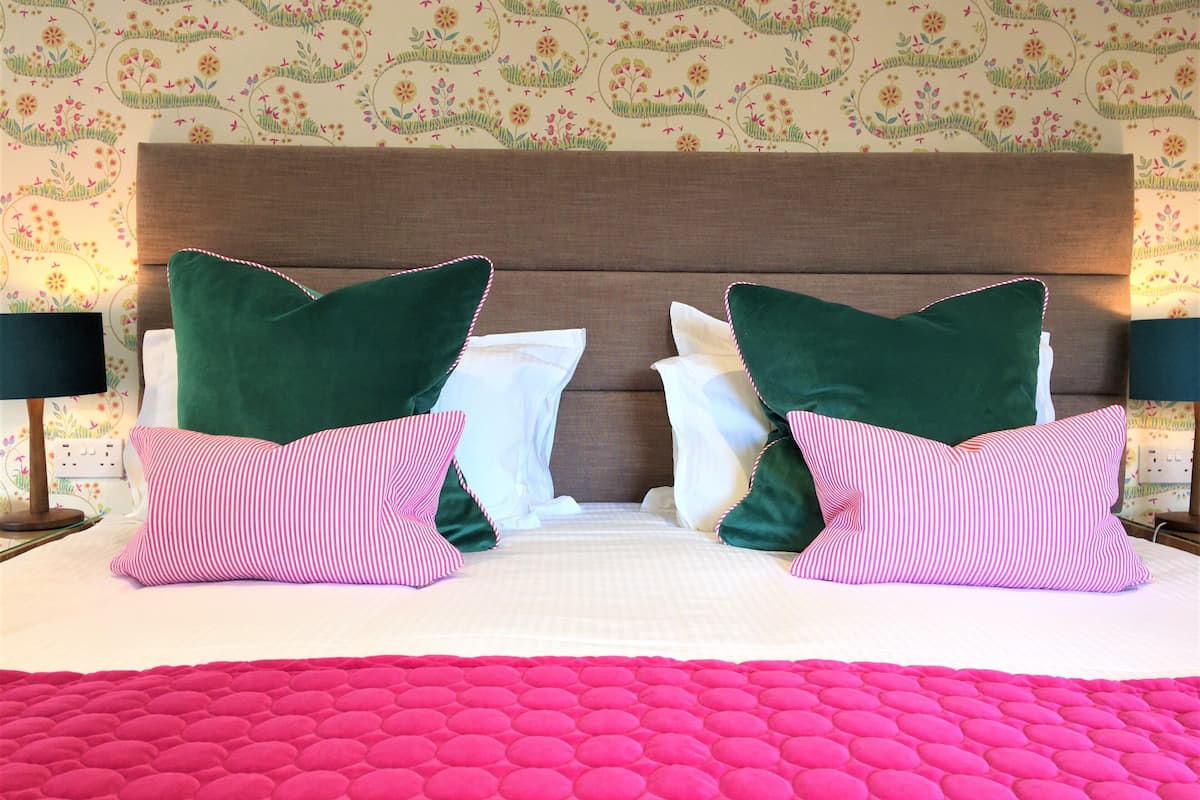 Un lit bien fait, avec une couette rose, deux oreillers verts et deux oreillers à rayures.