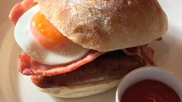 Un sandwich petit-déjeuner composé de jambon, de bacon et d’un œuf au plat, servi dans un pain et accompagné d’une portion de ketchup.
