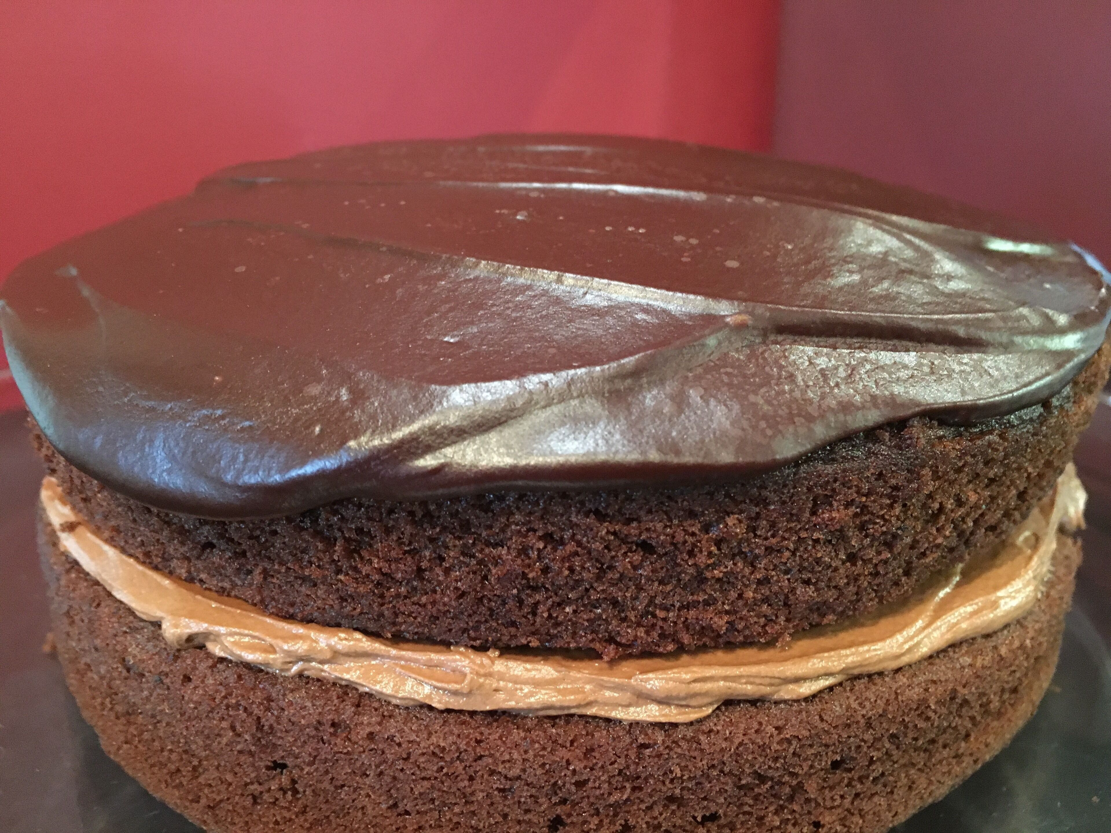 Una torta al cioccolato a strati con una glassa liscia al cioccolato sopra e uno strato di crema di arachidi all'interno.