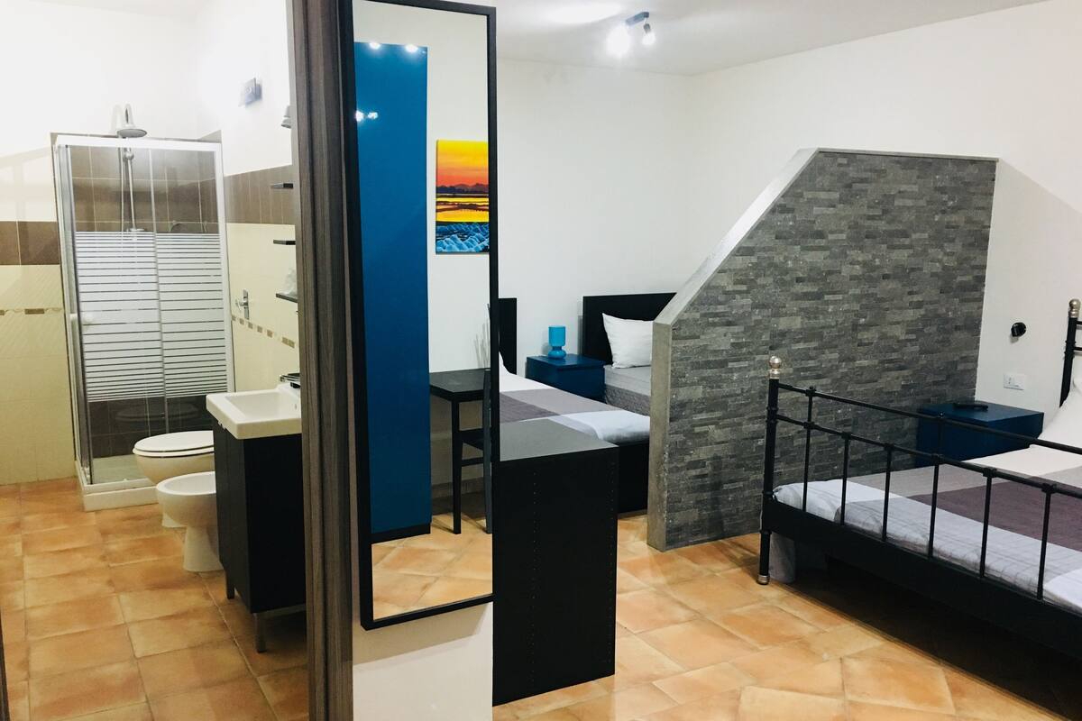 Habitación de hotel compacta con ducha, inodoro y cama con un pequeño escritorio.