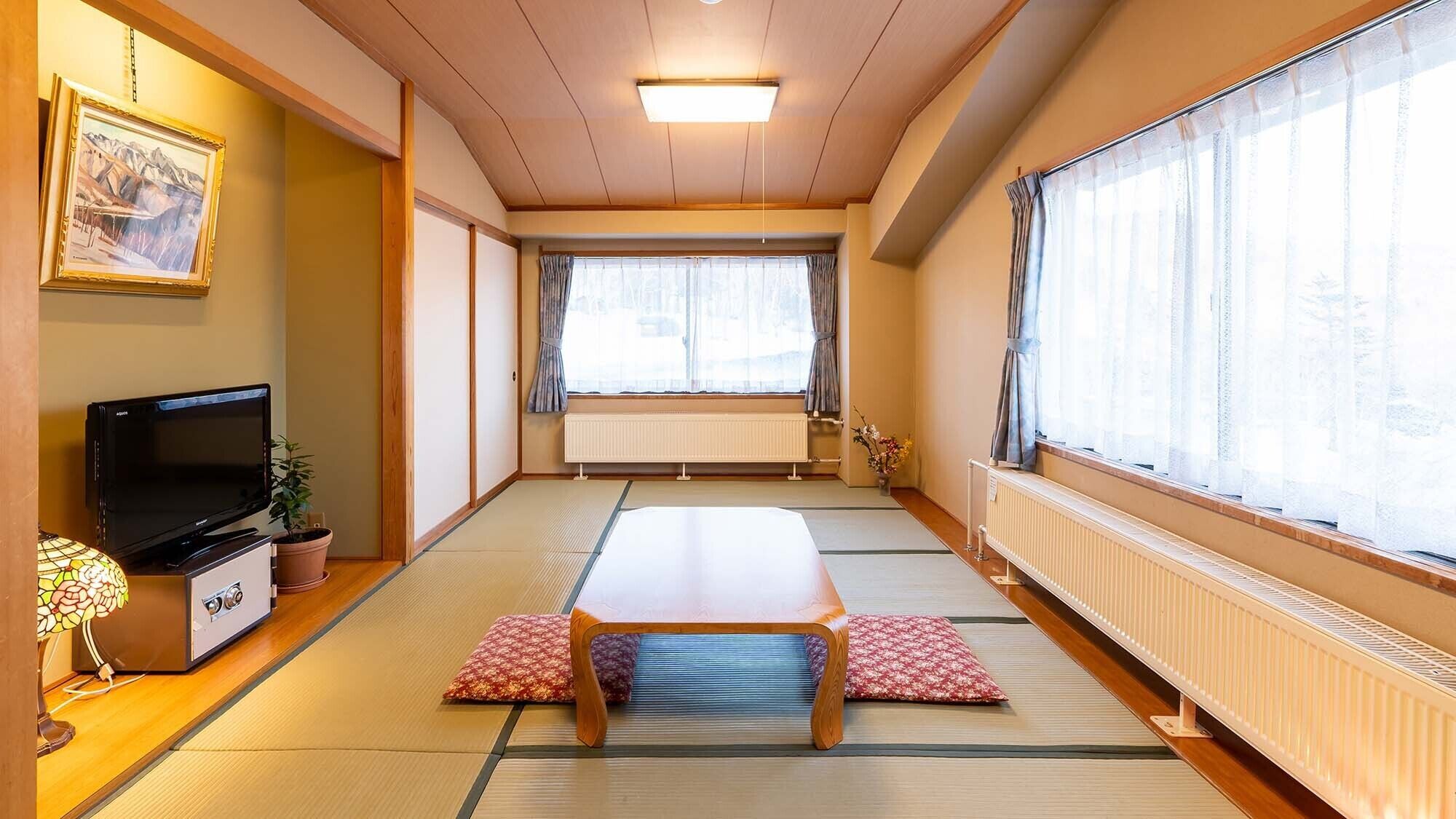 A traditional Japanese room with tatami flooring, a low table, a television, and a large window with curtains.