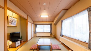 Una habitación japonesa tradicional con suelo de tatami, una mesa baja, un televisor y un radiador.