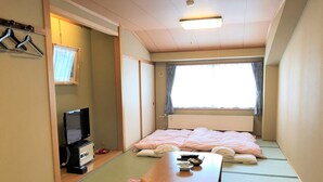 Una habitación japonesa tradicional con suelo de tatami, futón, televisor y una pequeña mesa con un cuenco y palillos.