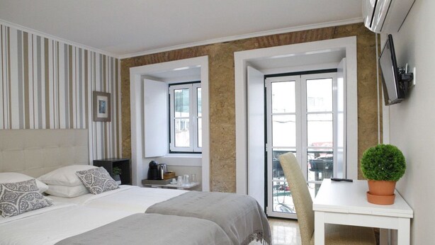 Une chambre d’hôtel moderne avec un grand lit, un bureau avec une chaise, une plante en pot et une vue sur la ville par la fenêtre.