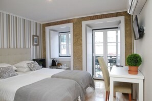 Een moderne hotelkamer met een groot bed, een bureau met stoel, een potplant en uitzicht op de stad door het raam.