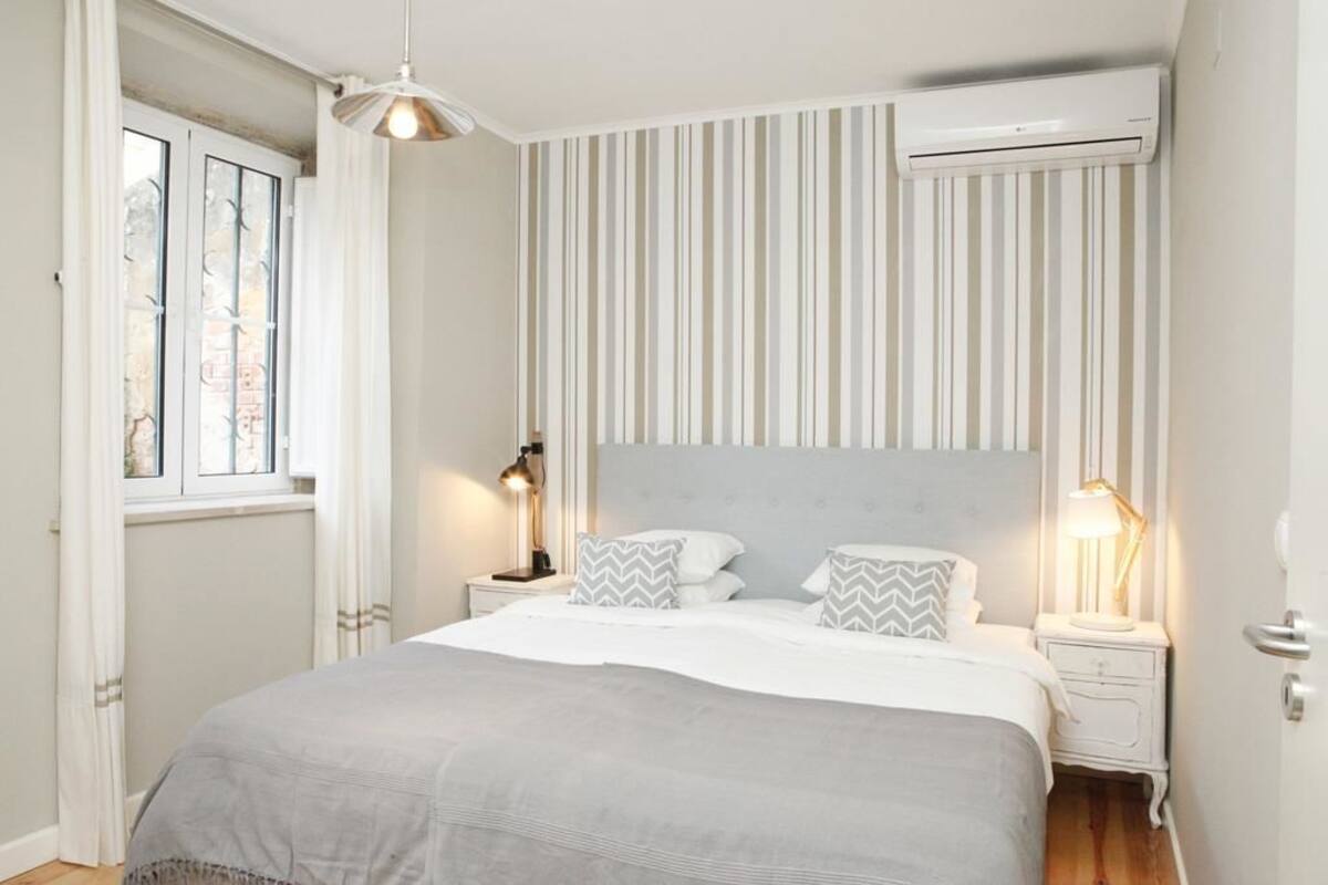 Een slaapkamer met een bed, twee nachtkastjes, een raam en een airconditioner.