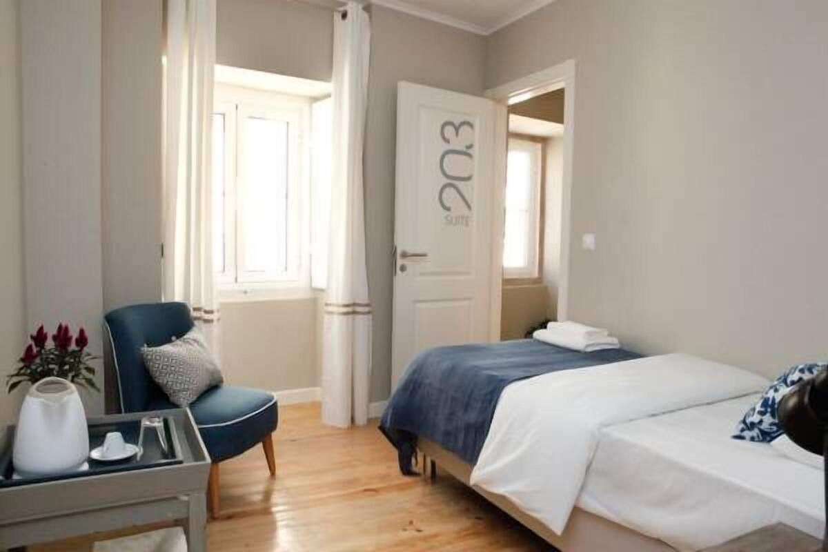 Hotelkamer met een bed, een stoel, een tafel met een vaas en een deur met daarop '203 Suite'.