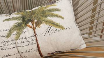 Almohada con diseño de palmera y texto escrito a mano, sobre una silla de estructura metálica.