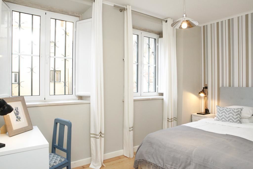 A bedroom with a bed, a nightstand, a chair, and a window with curtains.