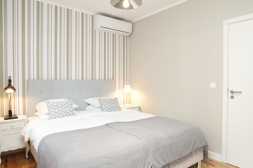 Une chambre à coucher comprenant un lit, des lampes de chevet, un climatiseur fixé au mur et une porte.
