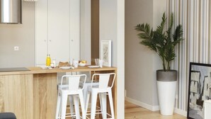 Une cuisine moderne avec un plan de travail en bois, des tabourets de bar blancs, une grande plante en pot et un mur à rayures.
