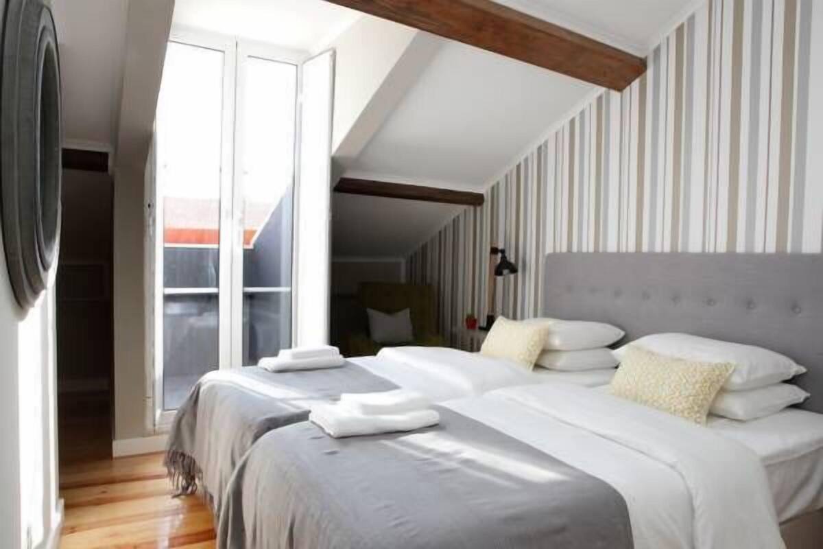 Een slaapkamer met twee bedden, een groot raam en een schuin dak.
