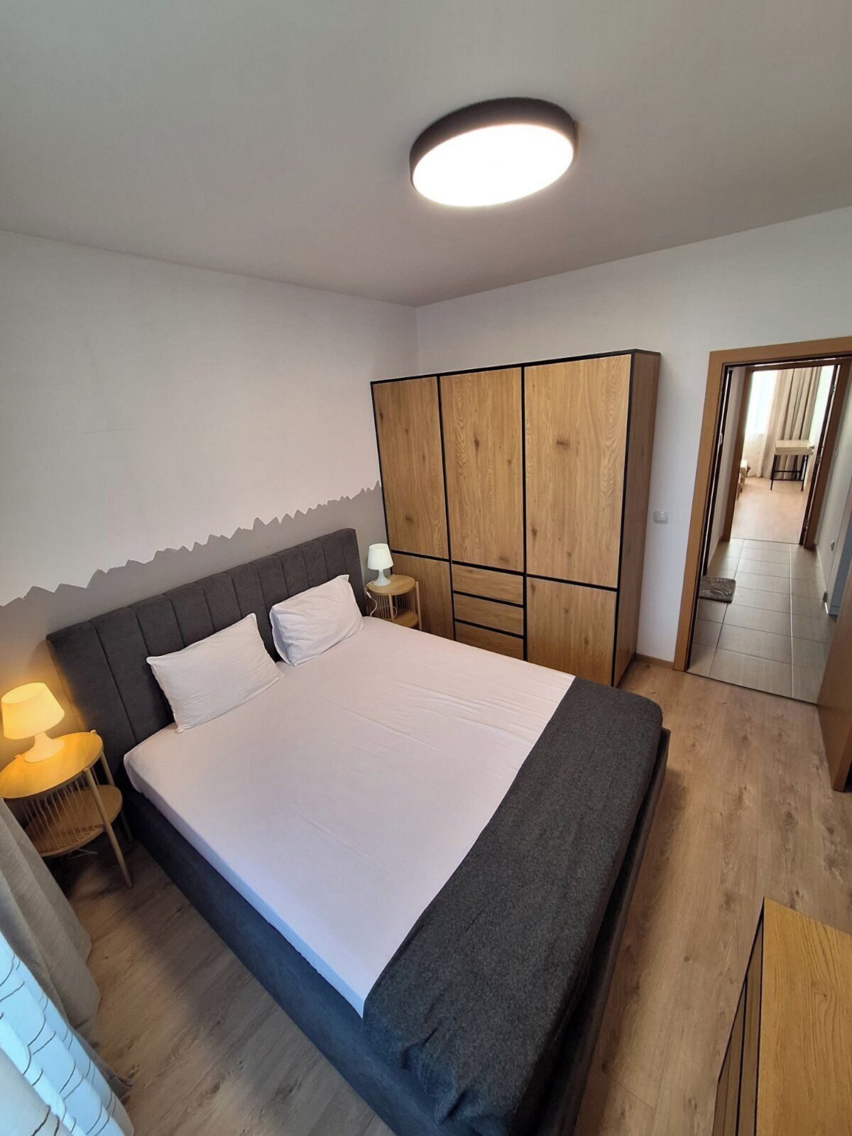 Un dormitorio con cama, mesitas de noche, armario y lámpara en el techo.