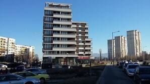 Un immeuble à plusieurs étages doté de balcons, d’un commerce au rez-de-chaussée et de plusieurs voitures garées.